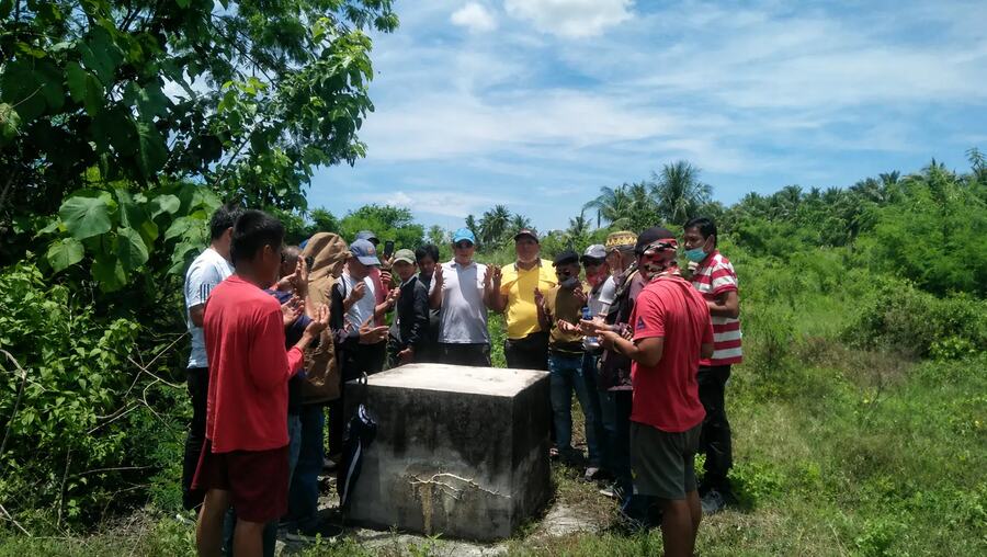 Community and field representatives gathered around a concrete well-site structure